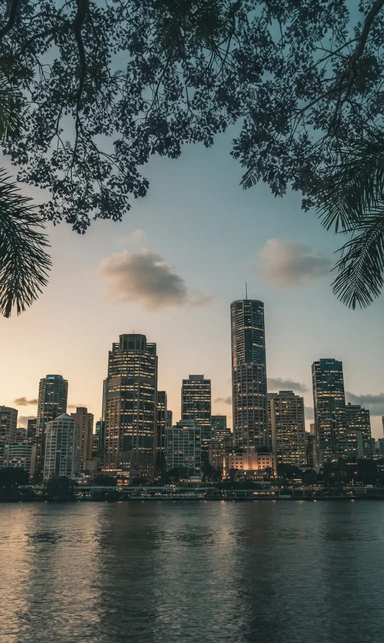 Brisbane's city skyline across the Brisbane River at dusk, framed by overhanging trees
